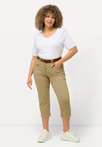 Top blanco de manga corta con escote en V, pantalones cortos beige con un cinturón marrón, combinados con zapatillas blancas. Tela suave y diseño ajustado visibles.