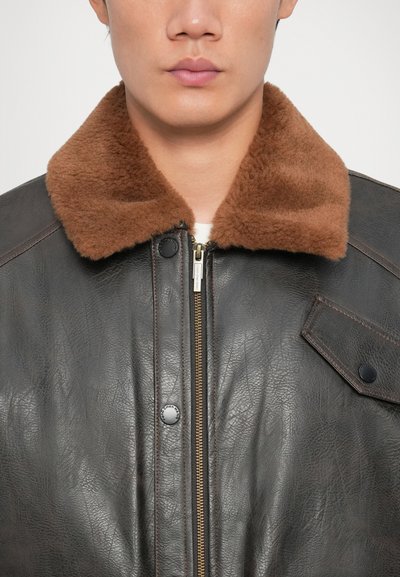 Brown leather jacket featuring a brown fleece collar, front zipper, and snap button details. Smooth texture with contrast stitching.
