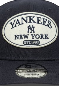 Gorra de béisbol azul marino hecha de tela con un parche blanco de fieltro. El parche presenta "YANKEES", "NUEVA YORK" y "EST. 1903" con un logo. Correa ajustable.