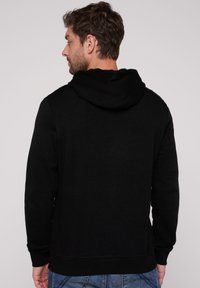 Sudadera negra con un acabado texturizado, que cuenta con una gran capucha, puños y cinturilla de canalé, combinada con unos jeans de mezclilla azules.