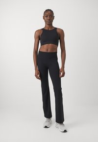 Μαύρο αθλητικό τοπ κοντό και ψηλής μέσης φαρδιά κολάν, κατασκευασμένα από λείο ύφασμα, συνδυασμένα με ελαφριά αθλητικά παπούτσια. Μινιμαλιστικός σχεδιασμός χωρίς σχέδια.