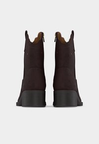 Καφέ σκούρα μποτάκια από σουέντ με χοντρές μαύρες τακούνια, διακοσμητικό ράψιμο και φερμουάρ στο πίσω μέρος, εμφανιζόμενα από πίσω σε λευκό φόντο.