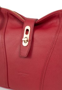 Borsa a tracolla in pelle rossa con superficie testurizzata, dotata di una cerniera dorata e di un importante dettaglio in metallo dorato sulla chiusura.