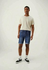 Donkerblauwe denim shorts met omgeslagen zomen, gecombineerd met een lichtbeige t-shirt met ronde hals. Draag het met zwarte sneakers en witte sokken.