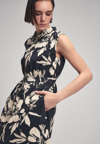 Navy blue without lengan floral dress dengan bunga krem, dilengkapi dengan kerah dan ritsleting di depan, pinggang yang meramping, dan saku samping.