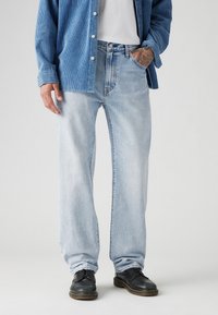 Lichtblauwe denim jeans met een rechte pasvorm, vervaagde textuur en zichtbare stiksels. Gecombineerd met zwarte, veterschoenen.