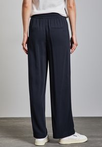 Pantaloni larghi blu navy realizzati in tessuto morbido; presentano un elastico in vita e due tasche posteriori; indossati con sneakers bianche.