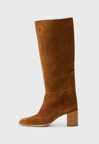 Botte en daim marron montée jusqu'au genou avec un bout arrondi et un talon en bois empilé, présentant une texture lisse et un design minimaliste.