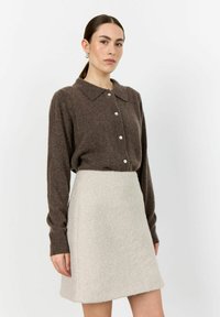 Brun ullblandad tröja med krage och knäppning, tillsammans med en ljusbeige utsvängd kjol i mjukt, texturerat tyg.