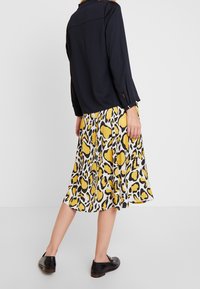 Zwarte blouse met lange mouwen en knoopmanchetten, gecombineerd met een knielange rok in geel en zwart panterprint en zwarte schoenen.