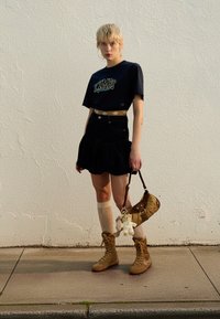 Navy graphic t-shirt, black denim ruffled skirt, beige knee-high socks, brown lace-up boots, and a small brown crossbody bag with a charm.
