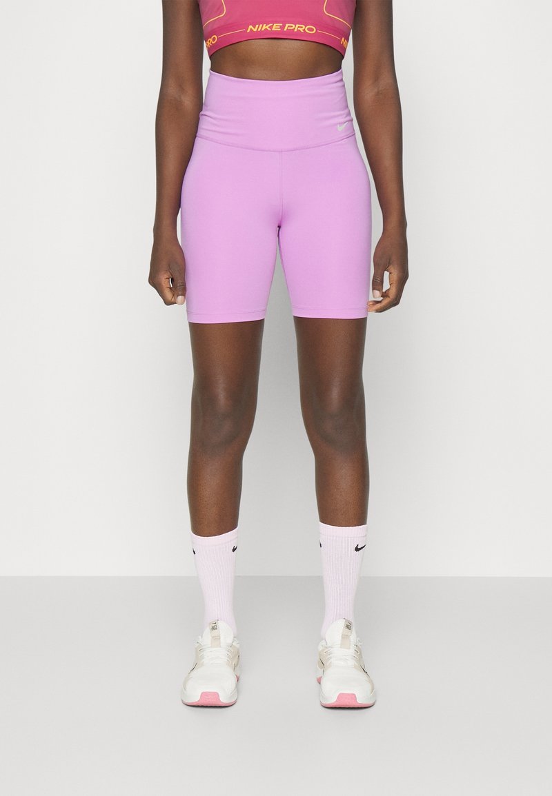 Shorts de sport violets à taille haute, associés à un haut court rouge Nike Pro et des chaussettes blanches Nike, portés avec des baskets claires.