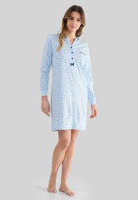 Camisón azul claro con mangas largas, pequeño patrón floral, tapeta de botones y un bolsillo frontal con un adorno de lazo. Tejido suave y ligero.