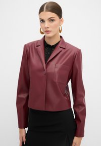 Blazer in finta pelle borgogna con un design su misura, chiusura a un bottone, rever a punta e taschino sul petto. Maniche lunghe, lunghezza cropped.