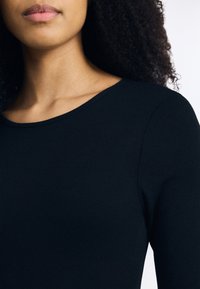 Camisola preta de manga longa com decote redondo, apresentando uma textura suave e um design ajustado.