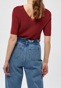 Czerwona krótka bluzka dzianinowa z dekoltem w kształcie V z tyłu, w zestawie z jasnoniebieskimi dżinsami z wysokim stanem, które mają elastyczny pas i dwie tylne kieszenie.