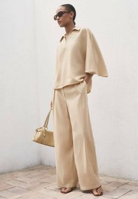 Beige, lösärmad blus med krage, tillsammans med vida byxor i samma färg. Tillbehören inkluderar en liten väska och solglasögon.
