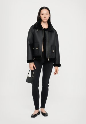 Veste en cuir noir avec un col en fourrure, fermeture éclair et poches latérales, associée à un jean skinny noir et des ballerines noires. Petit sac à main inclus.