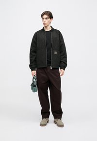 Μαύρο καπιτονέ μπουφάν bomber, απλό μαύρο t-shirt, φαρδιά μπορντό παντελόνια, πράσινη τσάντα χειρός και μπεζ μποτάκια με υφασμένες σόλες.