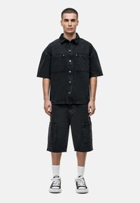 Chemise noire en denim à manches courtes avec devant à boutons et deux poches poitrine, assortie à un short longueur genoux. Design texturé et décontracté.