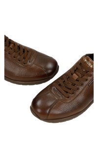 Sneakers in pelle marrone con punta rotonda, superficie texturizzata e allacciatura classica. Presentano una suola in gomma imbottita e un logo discreto sul lato.