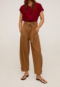 Haut bordeaux à manches courtes, associé à un pantalon marron taille haute, jambes larges, avec ceinture nouée et poches. Sandales plates.