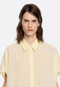 Yellow checkered short-sleeve shirt with a button-down front and a soft, lightweight texture. Features a classic collar and subtle buttons.