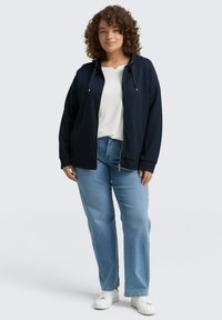 Sudadera navy con cremallera y cordones, combinada con una camiseta blanca y unos jeans de color azul claro. La tela parece suave, con un corte relajado y puños estándar.
