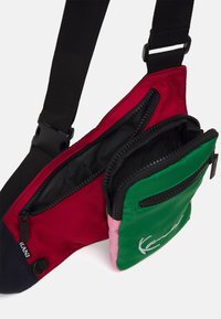 Kolorowa torba na ramię z czerwonym, zielonym i różowym wzorem. Przegrody na suwak z czarną podszewką i regulowanym paskiem. Trwała tkanina.