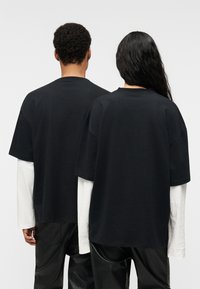 Μαύρα βαμβακερά T-shirts με άνετη εφαρμογή, κοντά μανίκια, στρογγυλές λαιμόκοψεις, φορεμένα πάνω από λευκά μακρυμάνικα μπλουζάκια. Μαύροι παντελόνες με υφή.