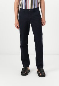 Námornícky modré nohavice so slim fit, vyrobené z bavlny. Obsahujú zapínanie na gombík a predné vrecká. Skombinované s čiernymi sandálmi na popruhy.