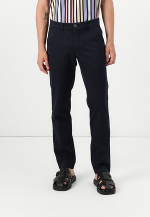 Mørkeblå bukser med slim fit, laget av bomull. Har knappelukking og forhånds lommer. Kombinert med svarte stroppsandaler.
