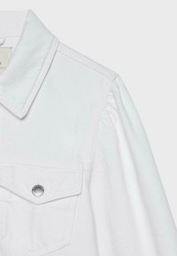 Gros plan de la partie supérieure d'une chemise blanche avec un col pointu et un rabat de poche maintenu par un bouton-pression argenté sur le côté gauche.