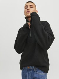 Pull noir en tricot avec un col haut et une fermeture éclair à moitié. Présente des poignets et un ourlet côtelés. Associé à un jean en denim bleu.