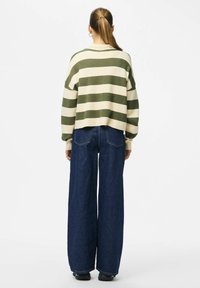 Pulover s črtami v olivno zeleni in krem barvi, krajši kroj. Kombiniran s širokimi temno modrimi kavbojkami z zadnjimi žepi in vidnim šivanjem.