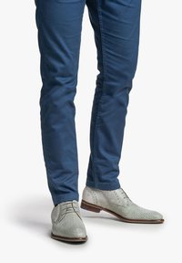 Zapatos de cuero texturizado gris claro con cordones y acentos perforados, combinados con pantalones azules ajustados. Enfoque en un diseño moderno y elegante.