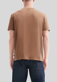 Camiseta de algodón marrón con cuello redondo y mangas cortas. Textura suave con un corte regular. Combinada con pantalones de mezclilla azul oscuro.