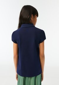 Korte mouw navy polo met kraag, gemaakt van gladde stof, met een gegolfde rand op de kraag, gecombineerd met een groene geplooide rok.