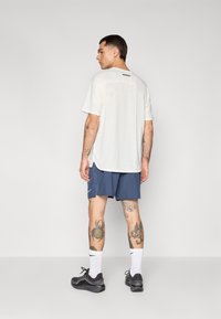 Lightweight, white athletic t-shirt with a textured back, paired with navy shorts. Features black brand logo and simple design.
