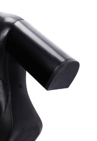 Black leather shoe with a rounded black heel. Heel has a textured, non-slip surface and smooth finish, displaying a clean, minimalist design.