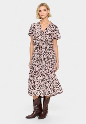 Blommig omlottkjol i svart med rosa blommor, korta ärmar och knytmidja. Matchad med bruna cowboyboots. Slät tyg och flödande kjol.