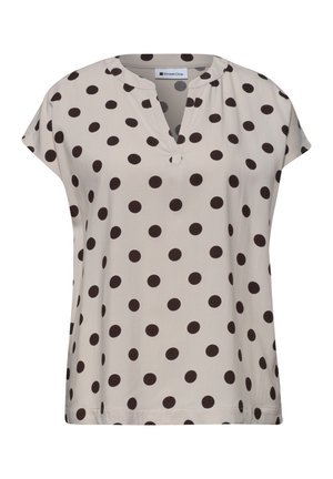 Blouse beige à manches courtes avec des pois noirs, encolure ronde avec une encoche en V et une coupe ample.