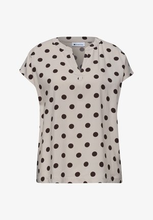 Blouse beige à manches courtes avec des pois noirs, encolure ronde avec une encoche en V et une coupe ample.