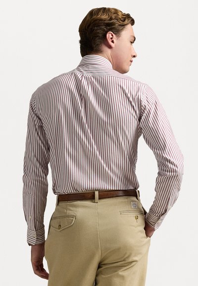 Chemise boutonnée à rayures rouges et blanches, avec un col ouvert. Associée à un pantalon kaki et une ceinture marron, mettant en valeur un design épuré.