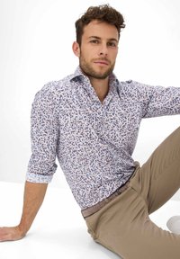 Blumenmuster-Hemd zum Knöpfen in Weiß mit blauen und braunen Akzenten. Kombiniert mit khakifarbenen Hosen und einem strukturierten braunen Gürtel.