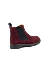 Stivali Chelsea in suede bordeaux con pannelli elastici neri, dettagli brogue e un interno in pelle marrone a contrasto con tacco impilato.