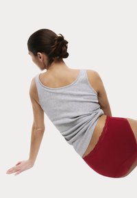 Szary bawełniany top na ramiączkach w połączeniu z czerwonymi, wysokim stanem majtkami z koronkową lamówką, przedstawiony z boku na jednolitym tle.