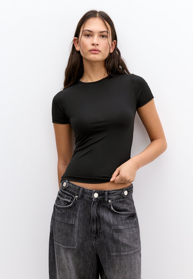 Black fitted t-shirt with short sleeves, smooth texture. Paired with high-waisted, slightly distressed dark denim jeans featuring button accents.