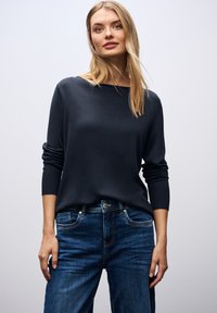 Marineblaues Sweater mit Bootsausschnitt und langen Ärmeln, kombiniert mit blauen Jeans aus Denim mit Fronttaschen und Knopfverschluss.
