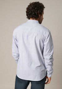 Lichtblauw overhemd met lange mouwen, voorzien van een klein geometrisch patroon, een doorknopen kraag en een afgeronde zoom. Gemaakt van katoen met een zachte textuur.